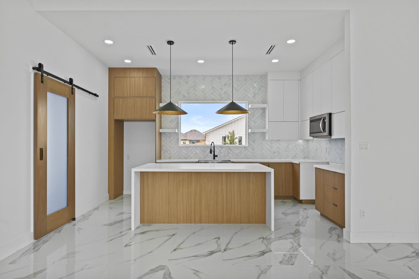 Interior entregado: cocina con azulejo en espiga, isla de roble y puerta corrediza de granero