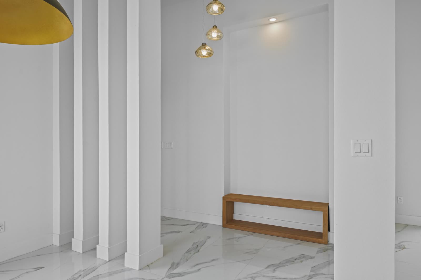 Interior entregado: vestíbulo con pilastras y banca de madera bajo nicho iluminado